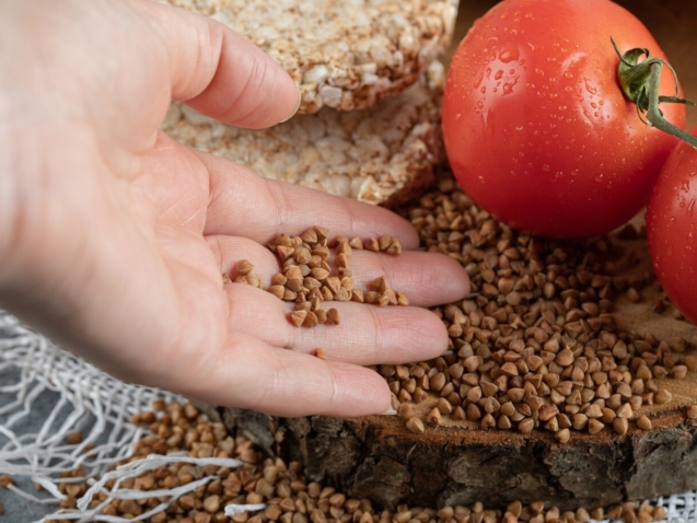 female-hand-holding-raw-buckwheat-from-wooden-piece_114579-25317